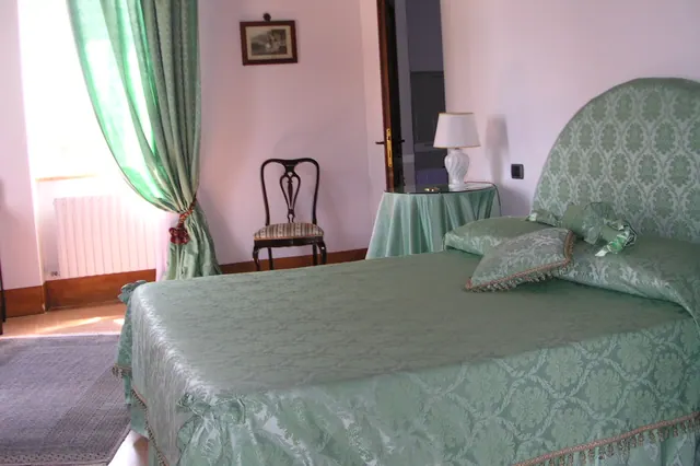 La camera Verde: letto matrimoniale con testiera e copriletto in damasco verde, tende abbinate e finestra luminosa