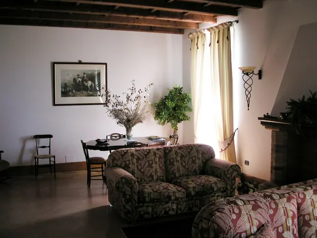 Il salotto degli ospiti con soffitto a travi di legno, divani, camino e un tavolo con fiori secchi