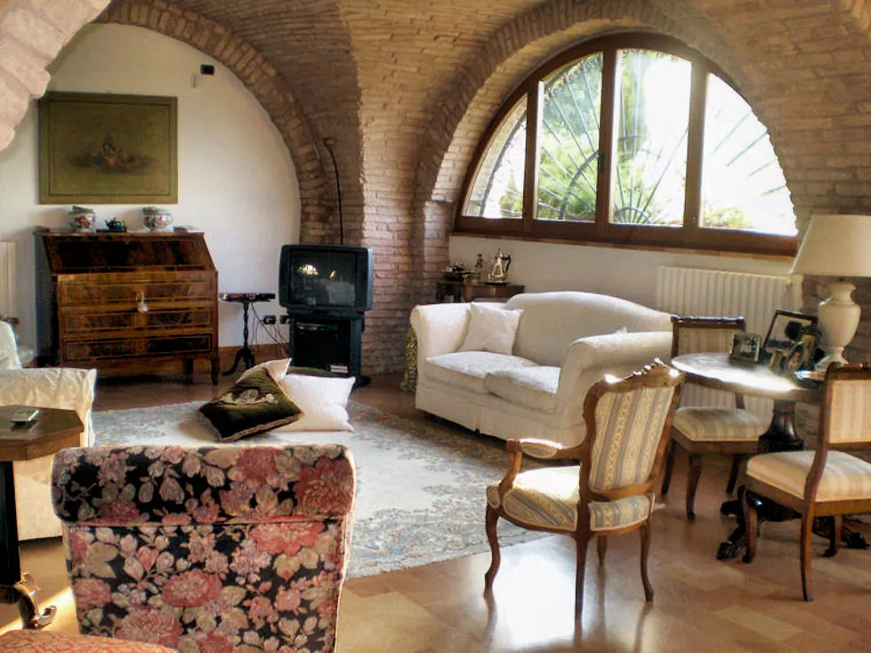Il salotto comune sotto le volte in mattoni, con divani, mobili antichi e la grande finestra ad arco sul giardino